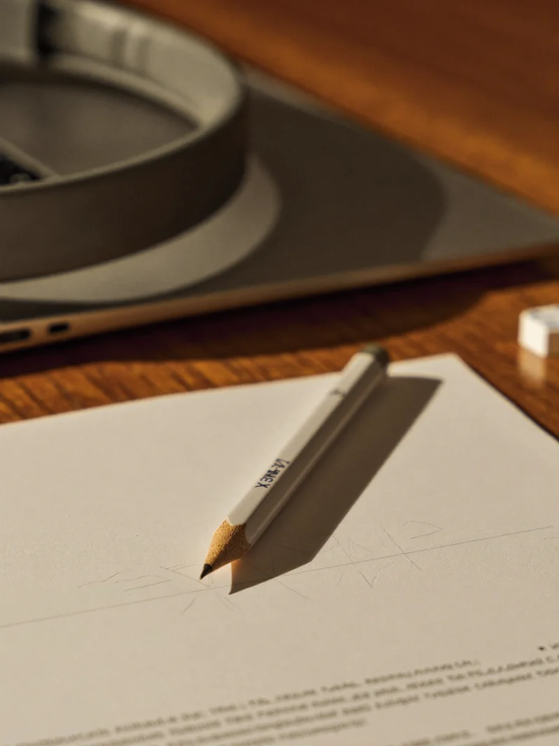 Durchgerechnetes Beispiel auf Papier mit Bleistift, Kopfhörer und Laptop im Hintergrund
